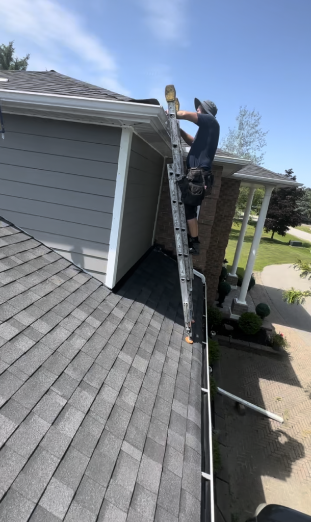 Technician working from a ladder placed on a lower roof to install drip edge on an upper roof section.