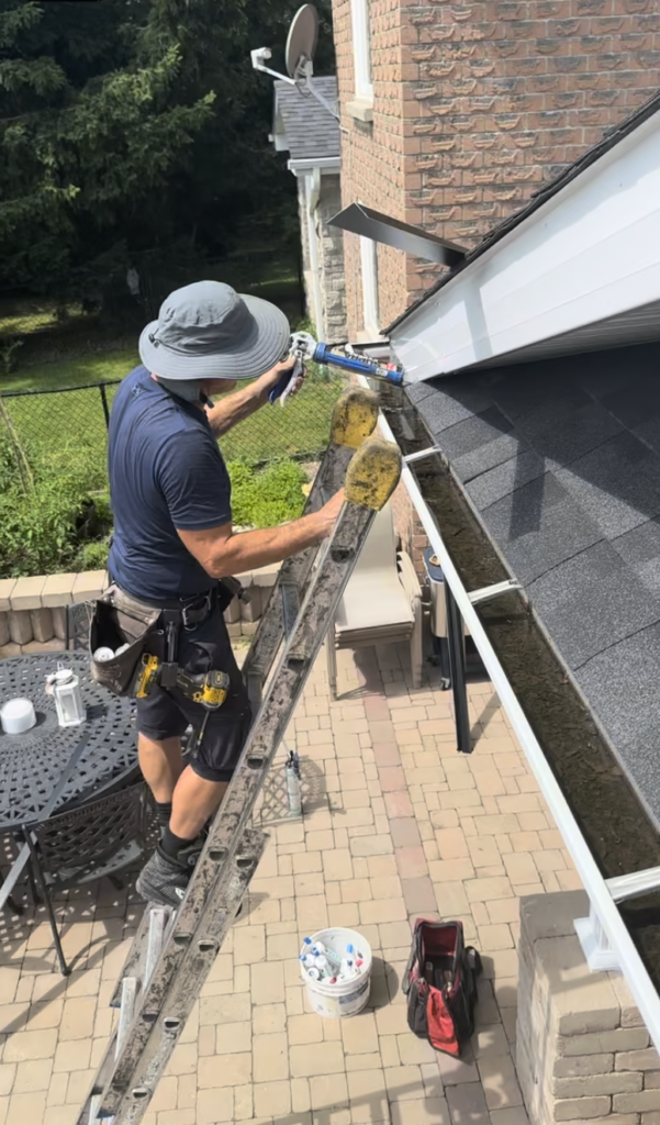 Technician installing custom drip edge at the roof edge while working from the top of a ladder on a multi-level home.
