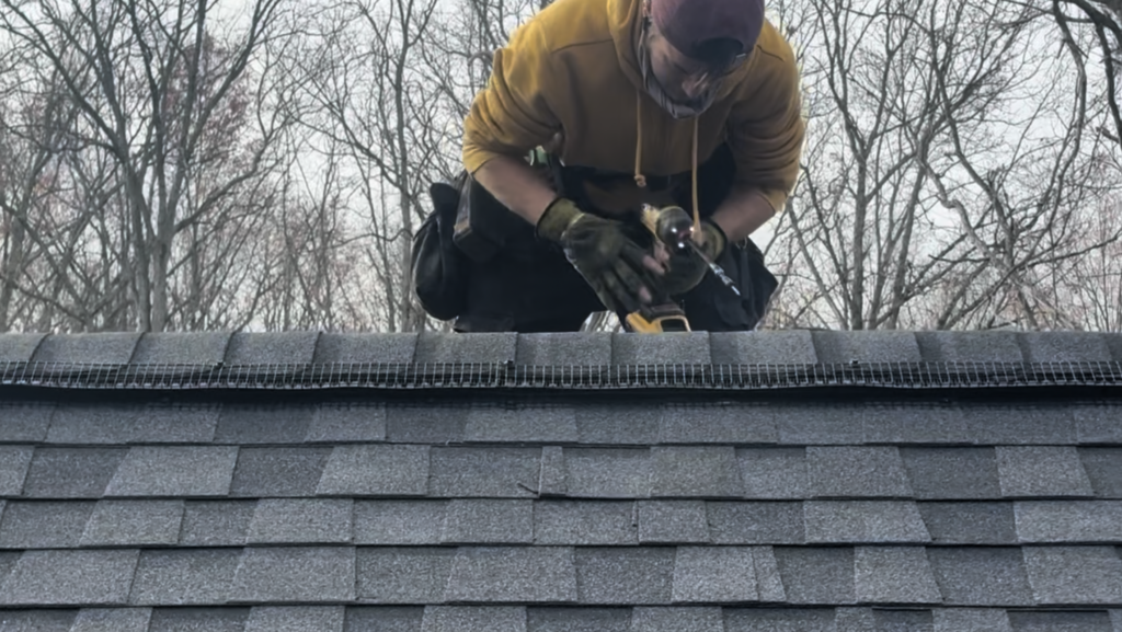 Technician installing custom bat-proof ridge vent screens beneath a roof ridge cap on an Ontario home.