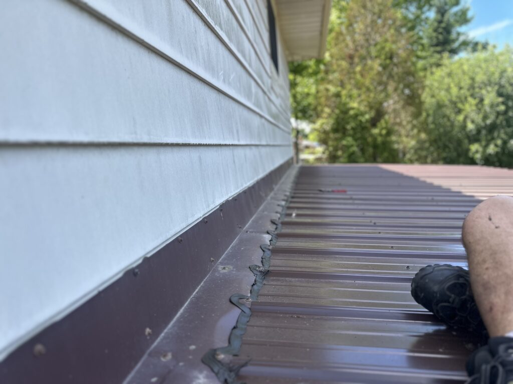 Metal roof wall flashing screwed down and caulked to seal gaps along the siding.